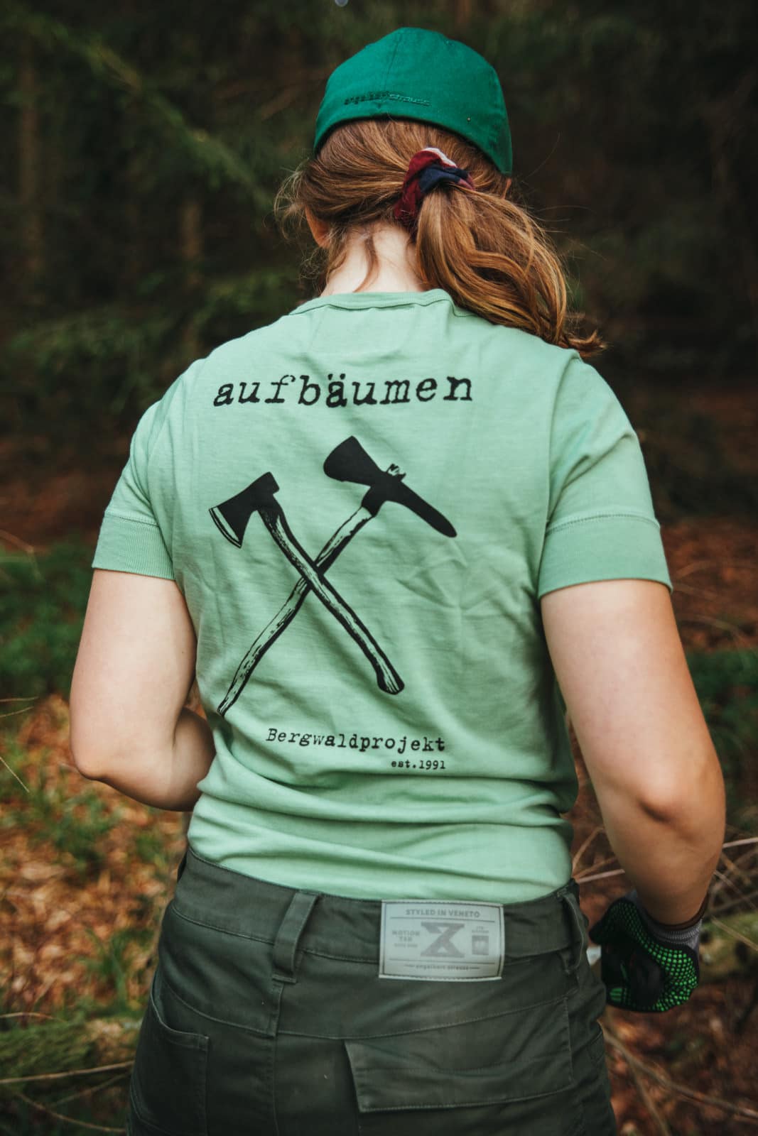 Junge Frau mit Bergwaldprojekt T-Shirt in grün mit der Aufschrift "aufbäumen" auf dem Rücken