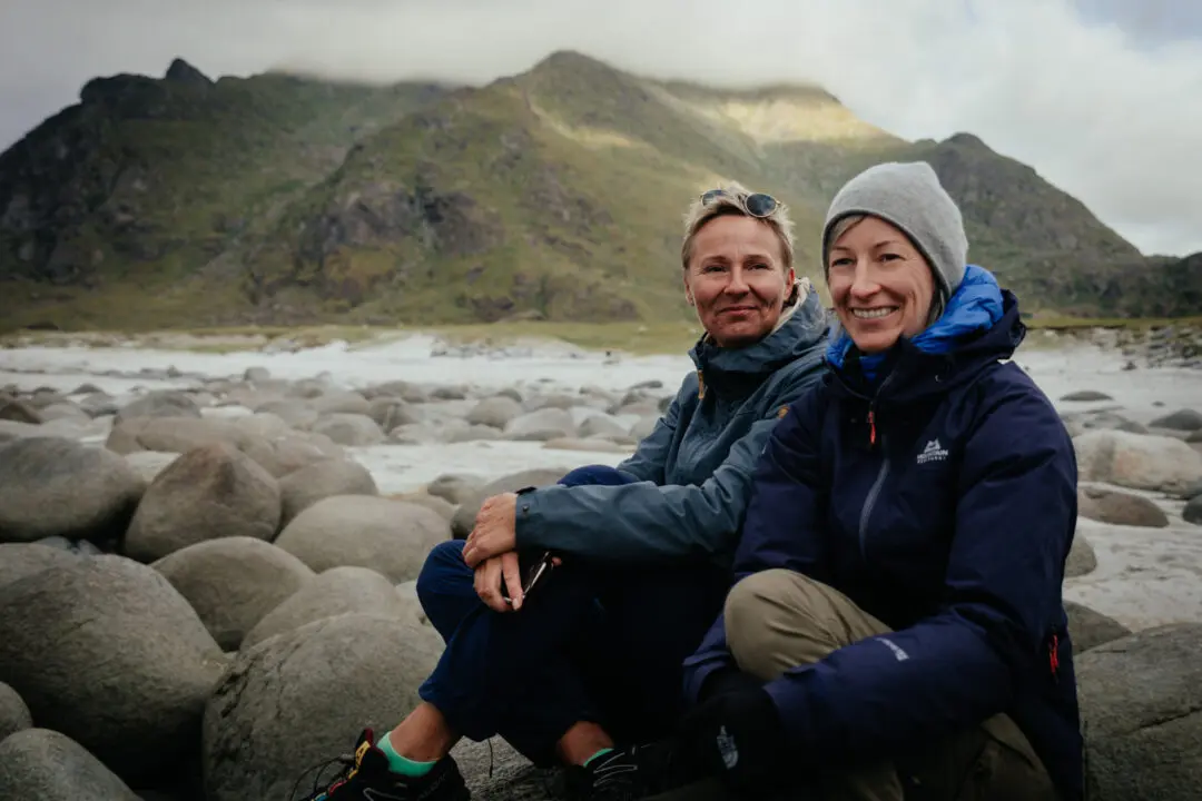 Zwei Frauen sitzen auf Felsen am Meer von Norwegen und lachen.