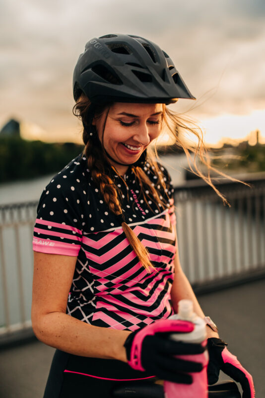 Frau in Fahrradbekleidung lacht mit Sonnenuntergang