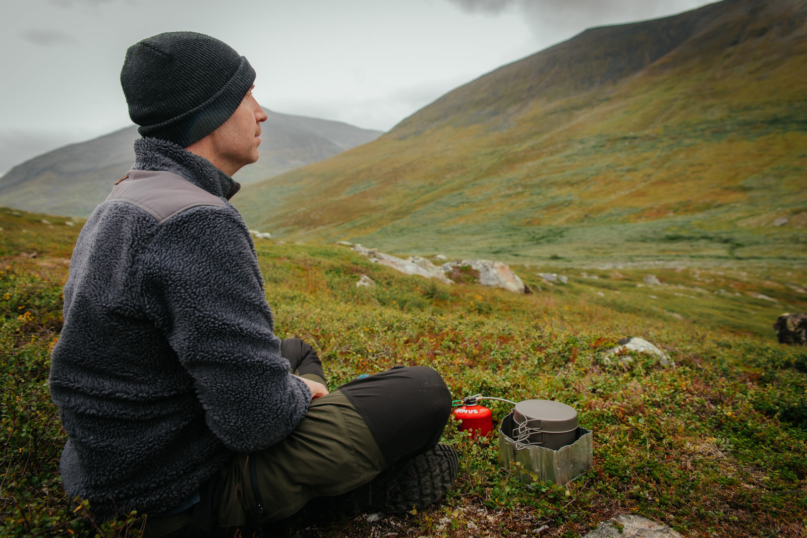 Mann kocht Essen auf dem Kungsleden mit Ausblick auf die grünen Berge